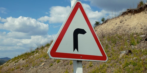A white arrow with an angle bend in it is painted onto a grey paved raod  A white arrow with an angle bend in it is painted onto a grey paved raod